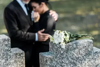 People hugging by a gravesite covered with flowers