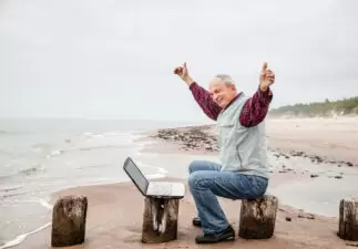 Happy old man with a laptop on the beach on a foggy day