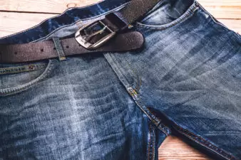 Blue jeans with a leather belt spread on ground