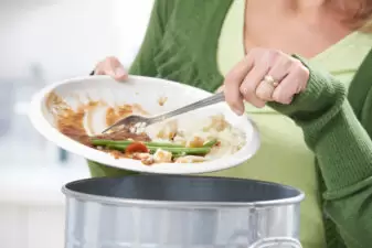 woman scraping food off a plate into the garbage