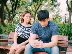 Jealous girlfriend peeking and spying her boyfriend mobile phone while he is reading a message