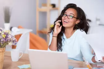 Happy young woman on her laptop while talking on the phone