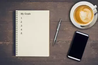 A notebook with "My goals" written at the top next to a pen, phone, and cup of coffee