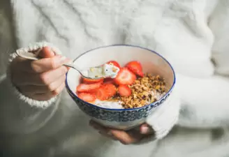 Woman eating bowl of granola, yogurt, and fruit in bowl