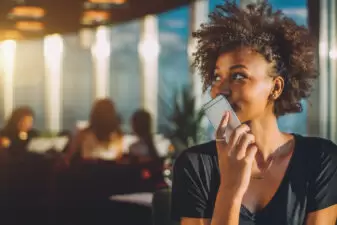 Black woman with curly hair holding her mouth over her phone