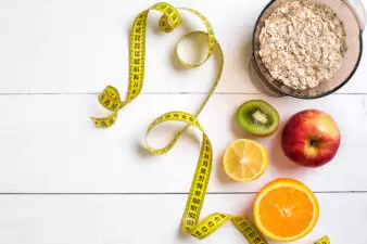 Fitness concept with fruit, bowl of oatmeal and centimeter. Top view background concept.