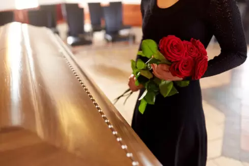 woman with red roses and coffin at funeral