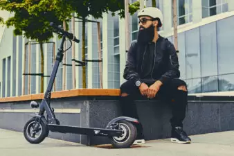 Bearded man sitting next to electric scooter