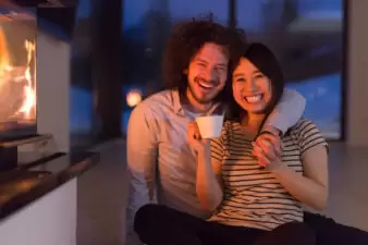 happy multiethnic couple sitting in front of fireplace