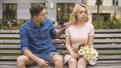 Young man feeling guilty with girlfriend on bench