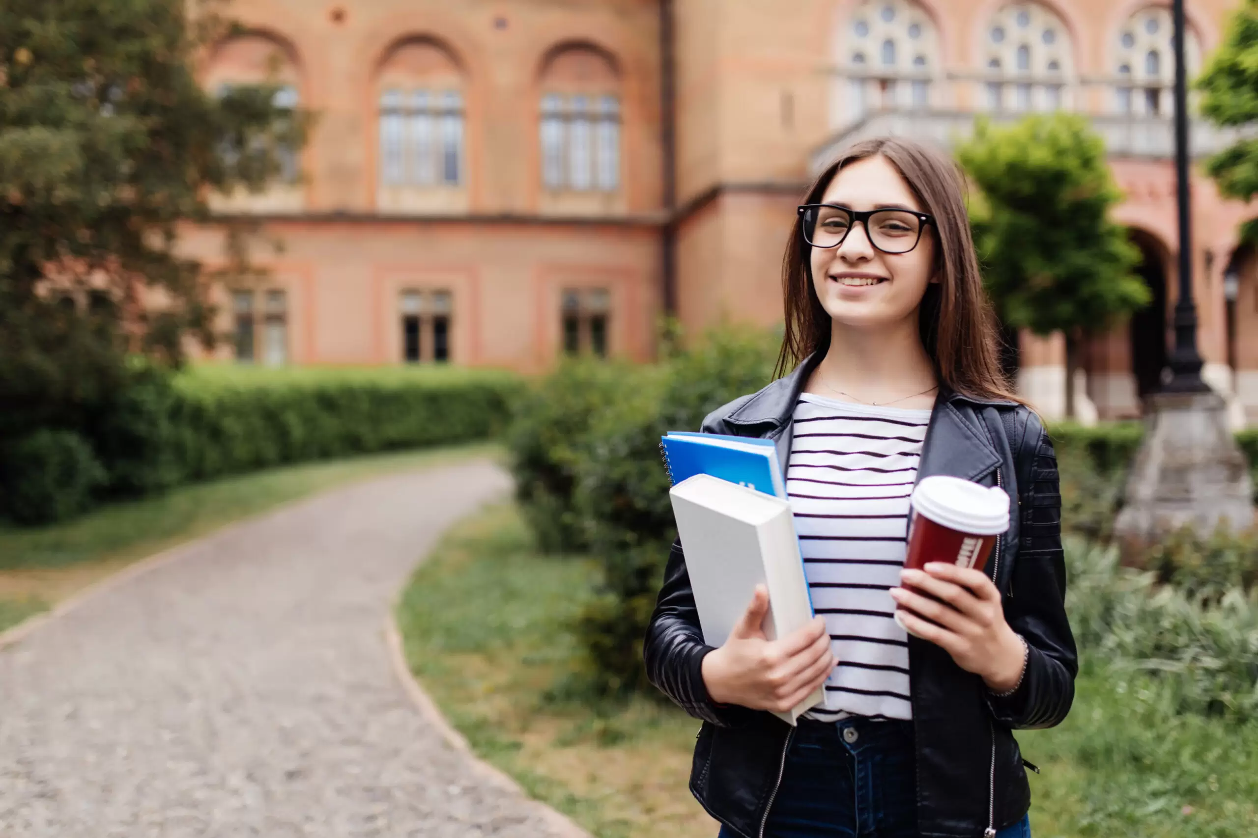 American university student smiling with coffee and book bag on campus