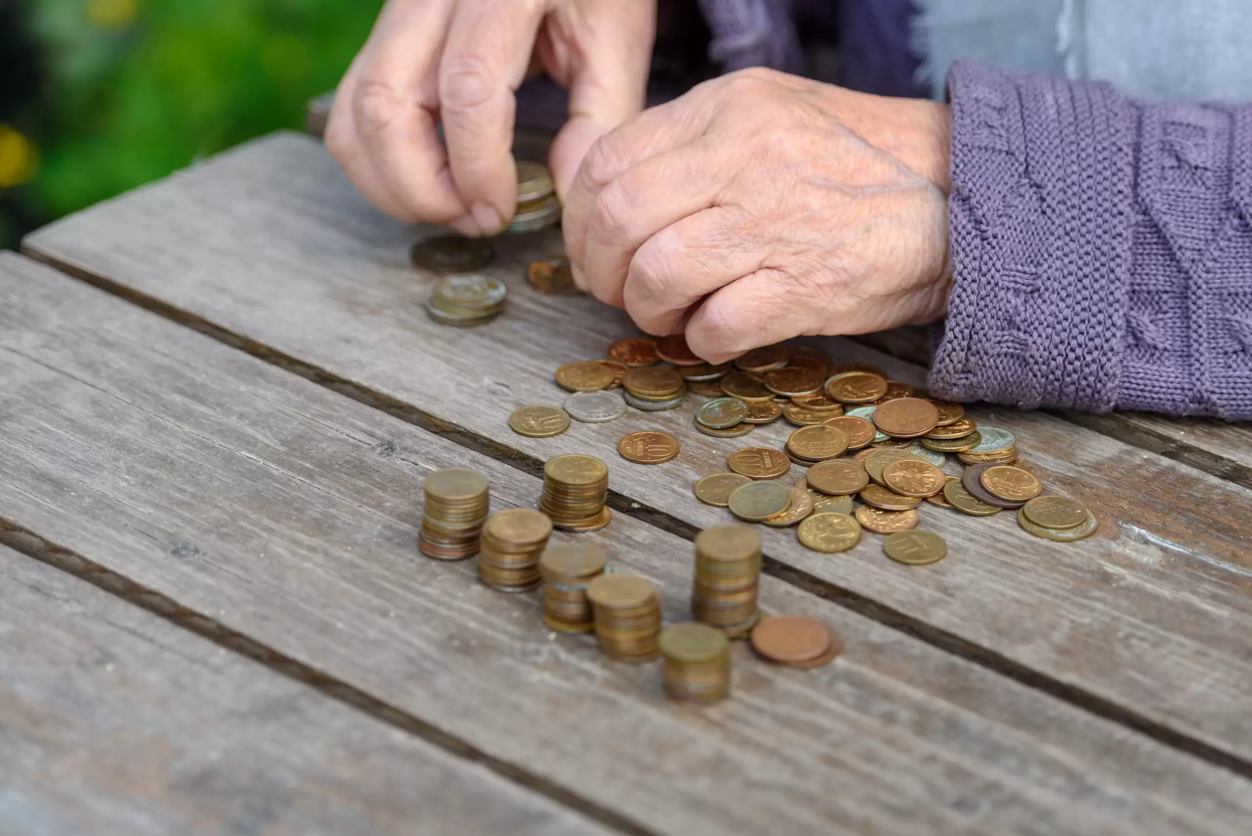 wrinkled hands of the old woman touch coins on a wooden table