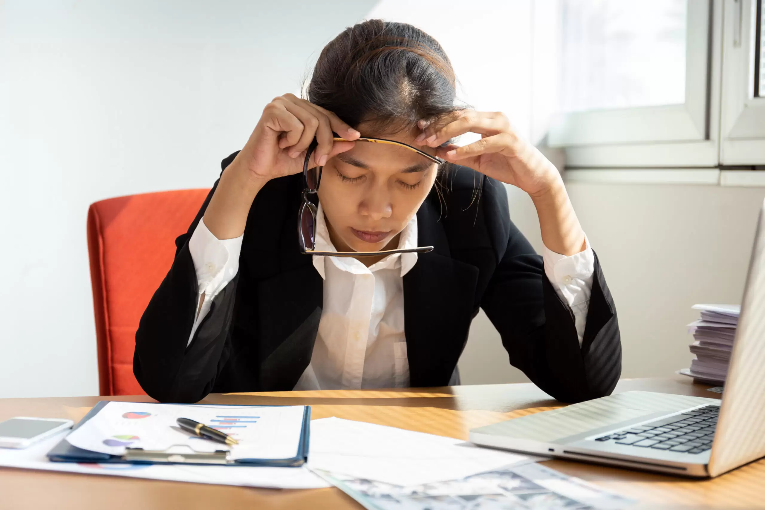 Businesswoman resting hands on head with eyes close at work desk in office.