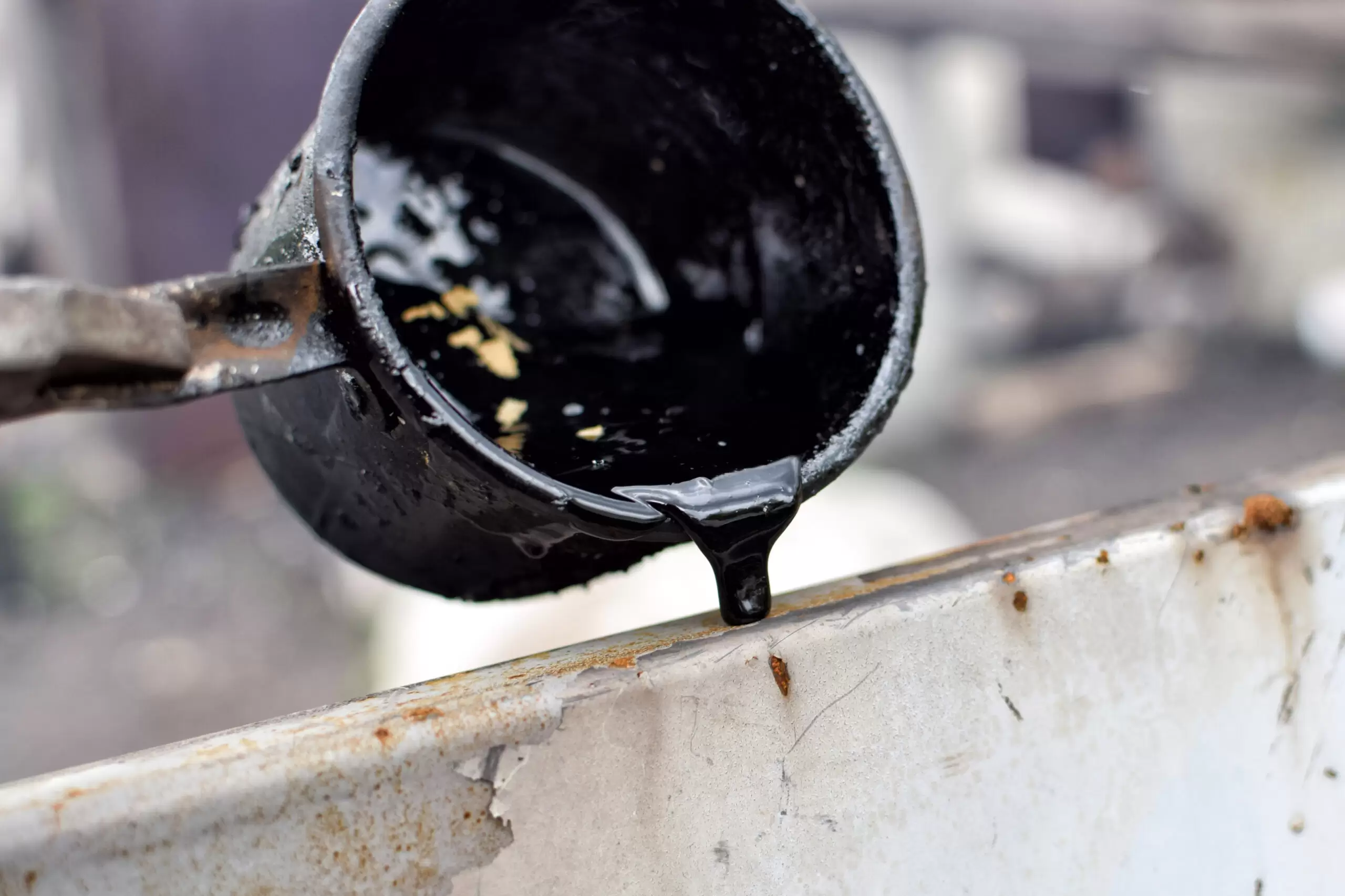 Outflow of melted hot black tar from metal cup on surface with steam