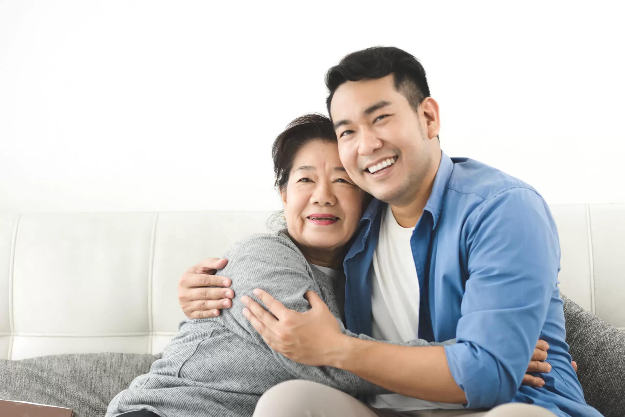 Asian mother hugging her son and sitting on sofa at home