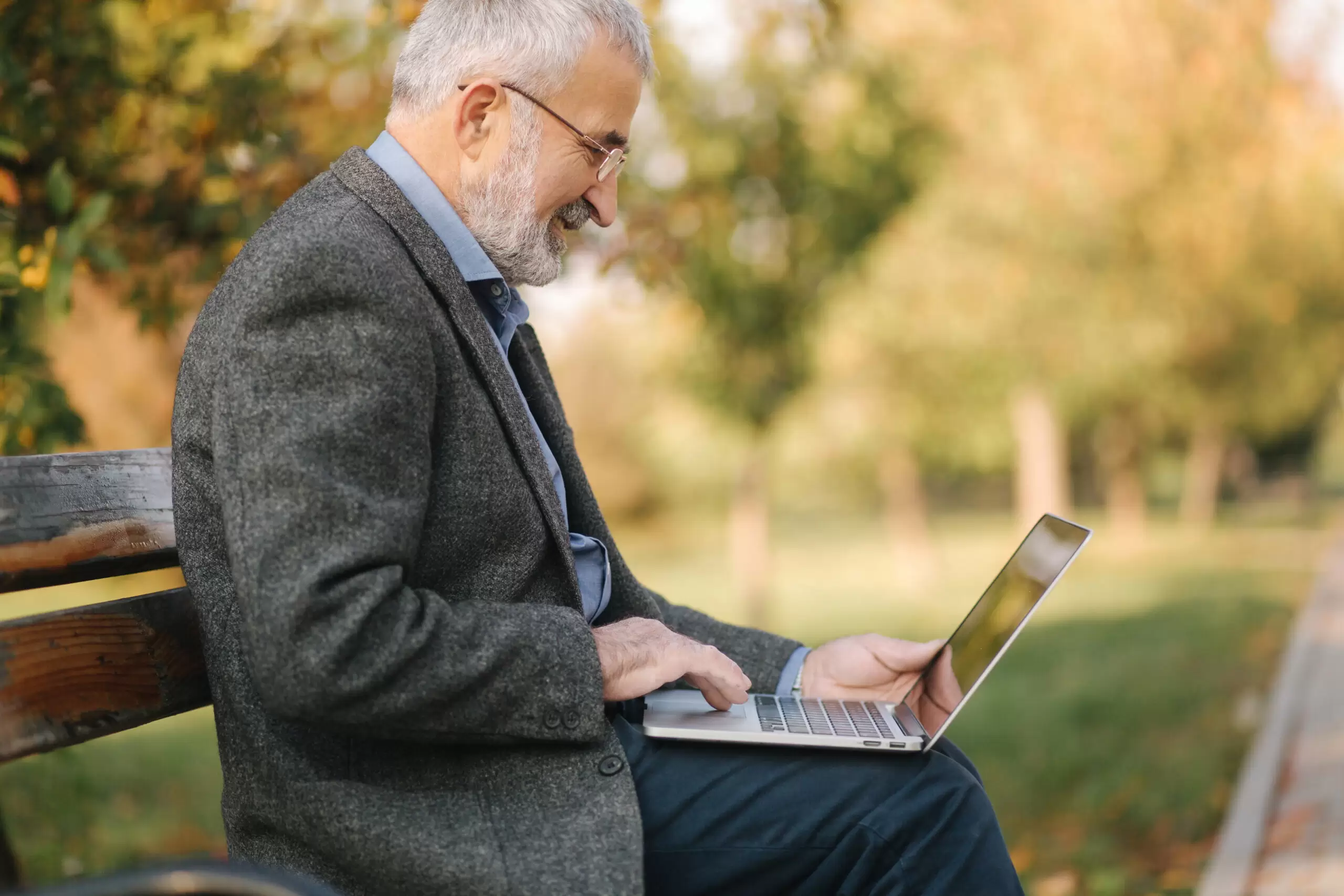 Elderly man use laptop in the park. Handsome senior man in glasses work outside