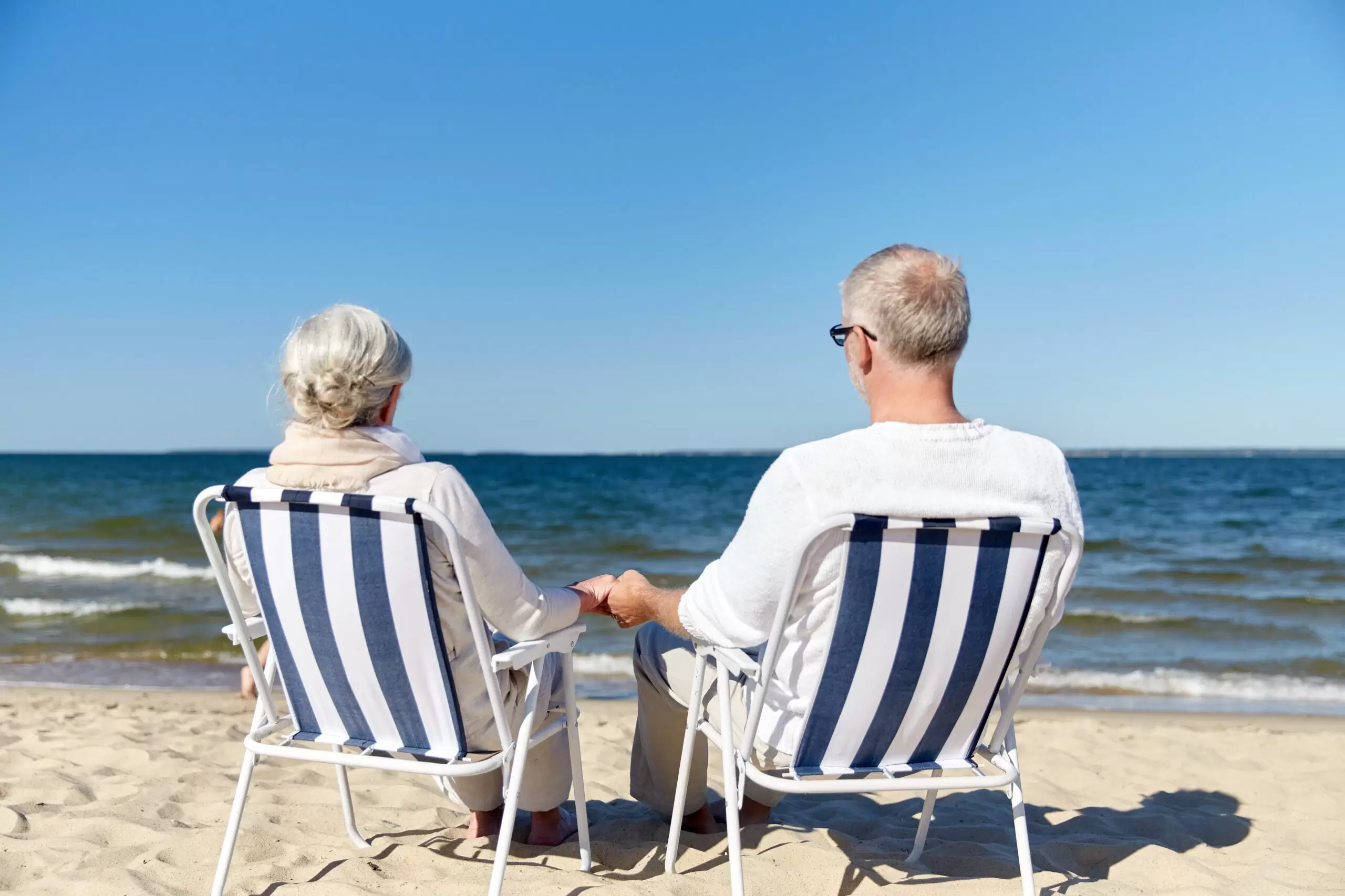 senior couple sitting on chairs at summer beach