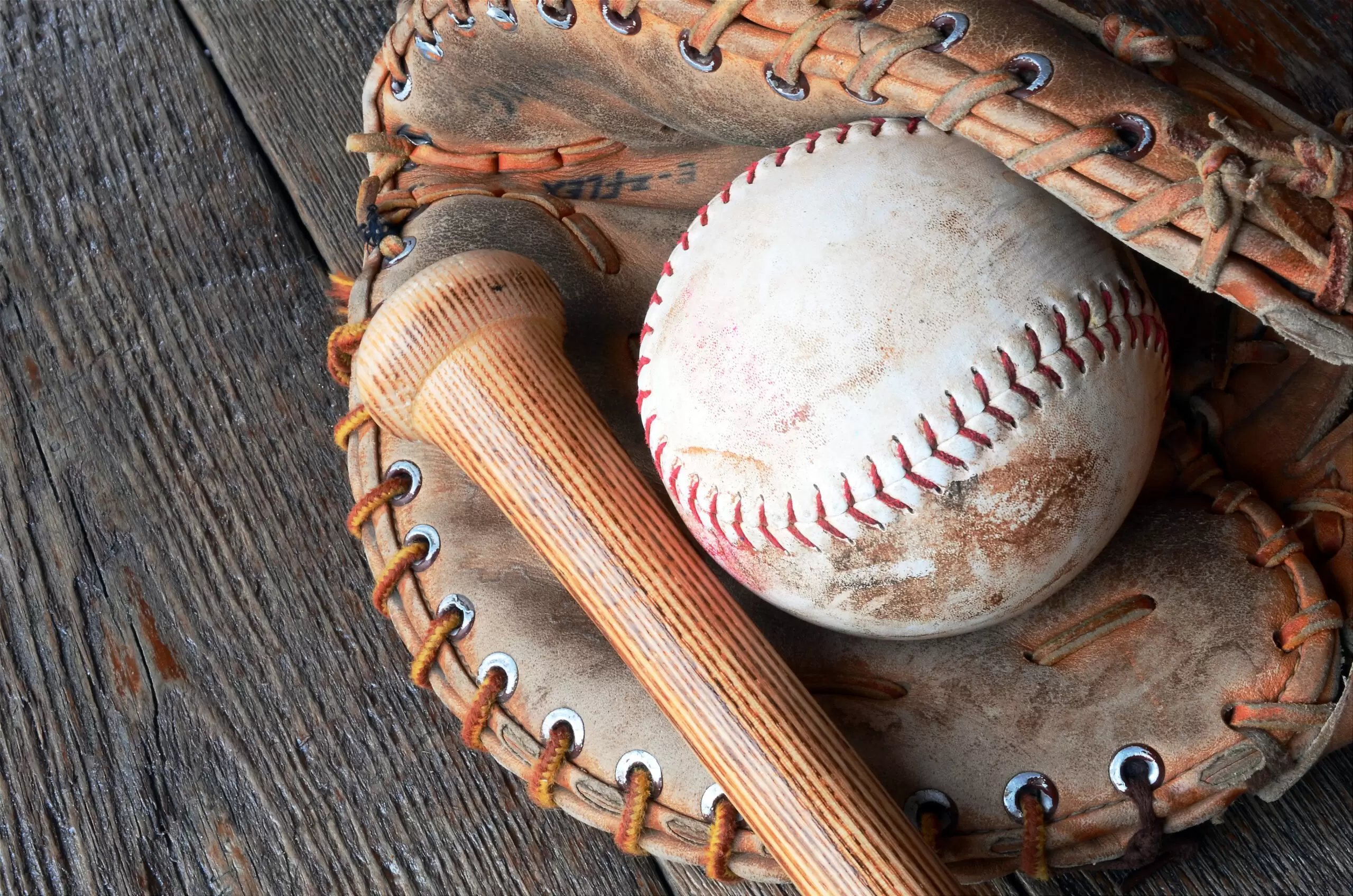 Close up image of baseball glove, ball, and wooden bat