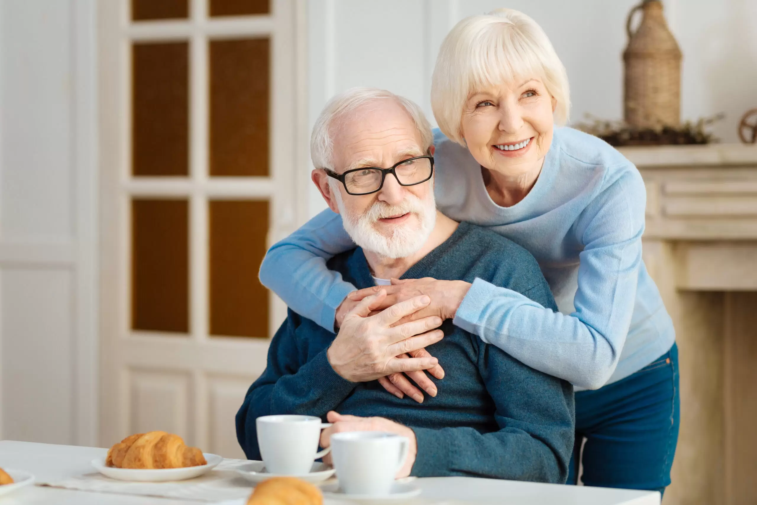 Blonde older woman hugging her husband at breakfast table