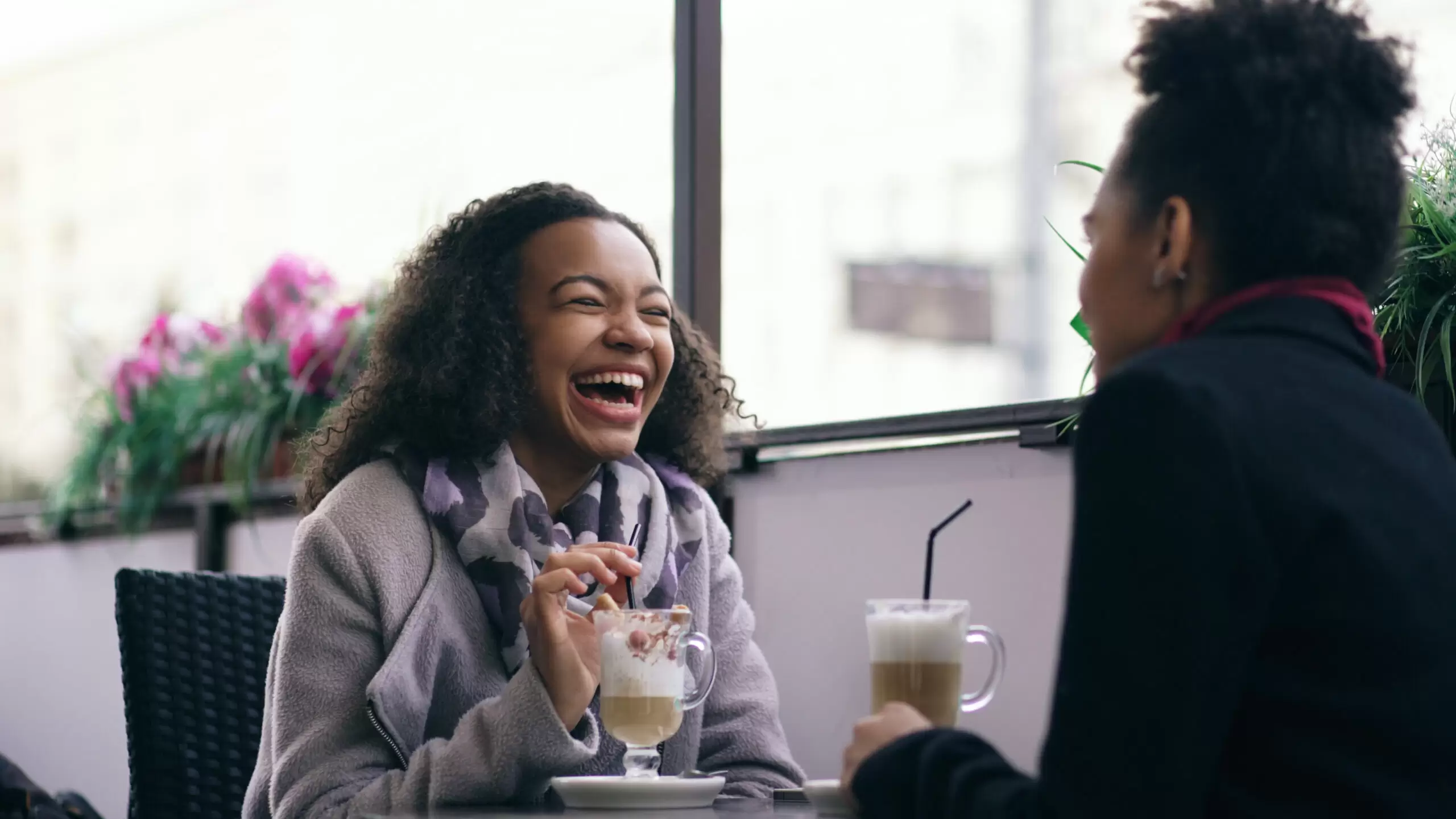 Two women laughing and talking over drinks